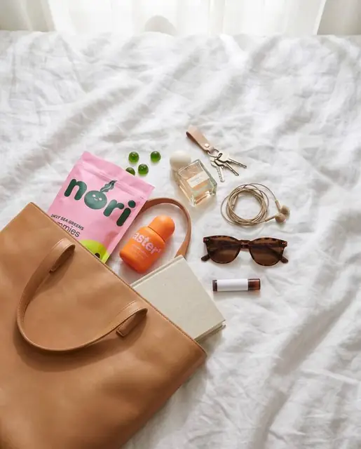 A flatlay of a bag, notebook and sunglasses